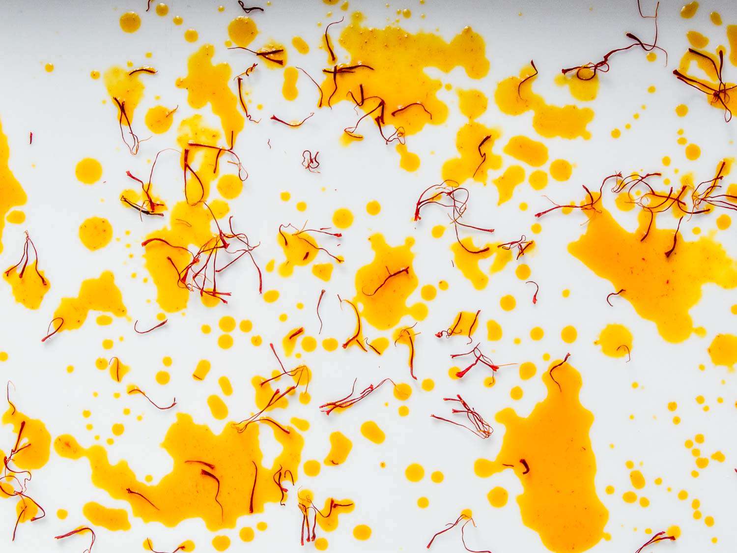 Close-up of threads of saffron and splattered saffron "tea" dispersed on a white surface.