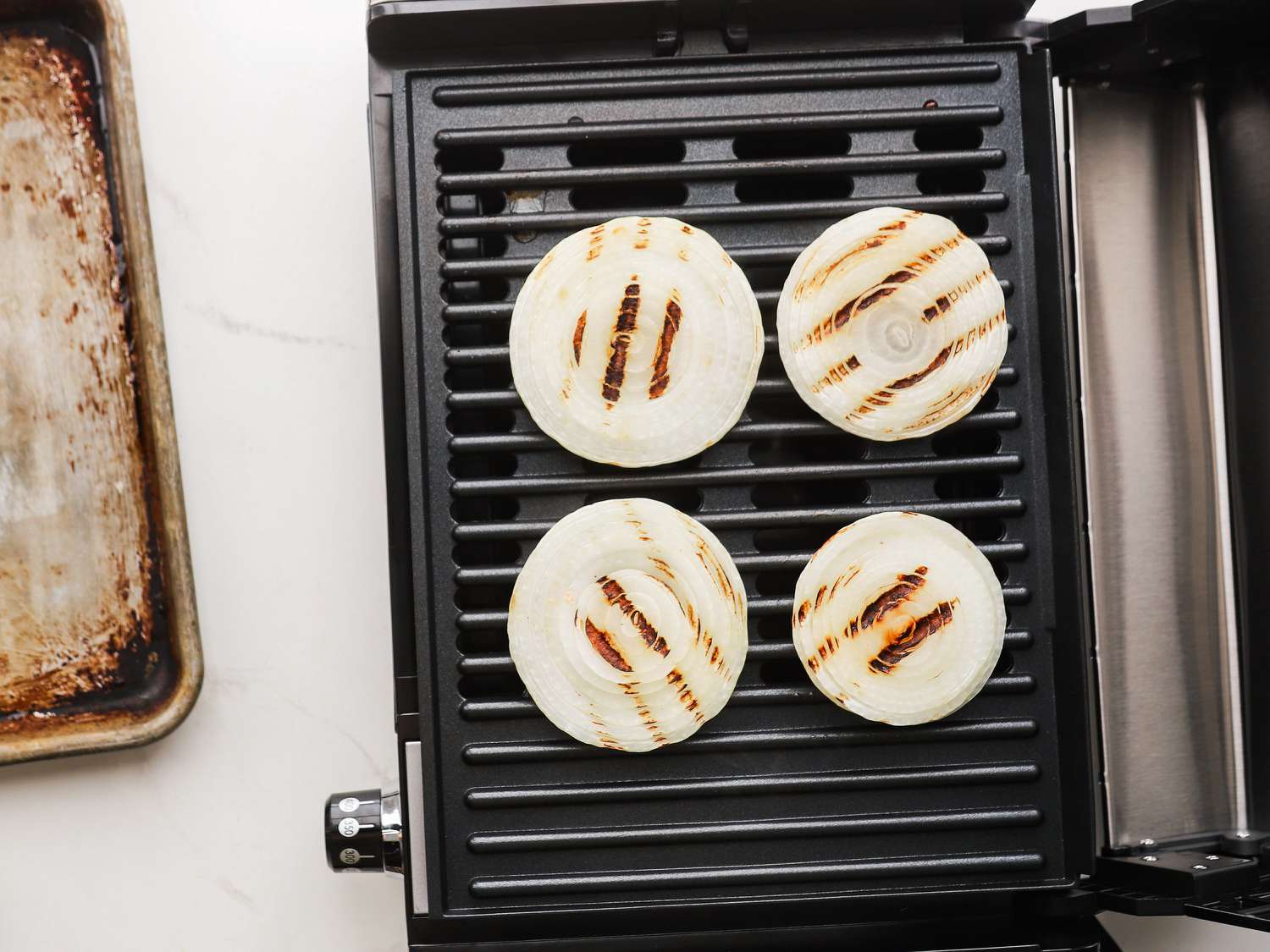 Onions cooking on an indoor grill next to a sheet pan