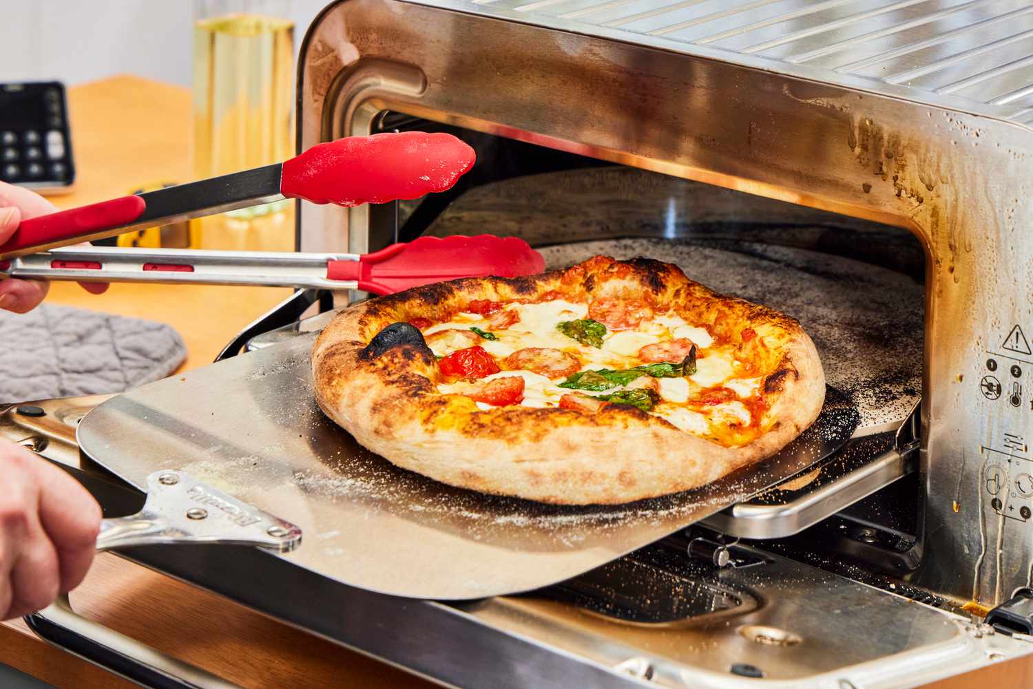 A person removes a pizza from the Breville Smart Oven Pizzaiolo Pizza Oven