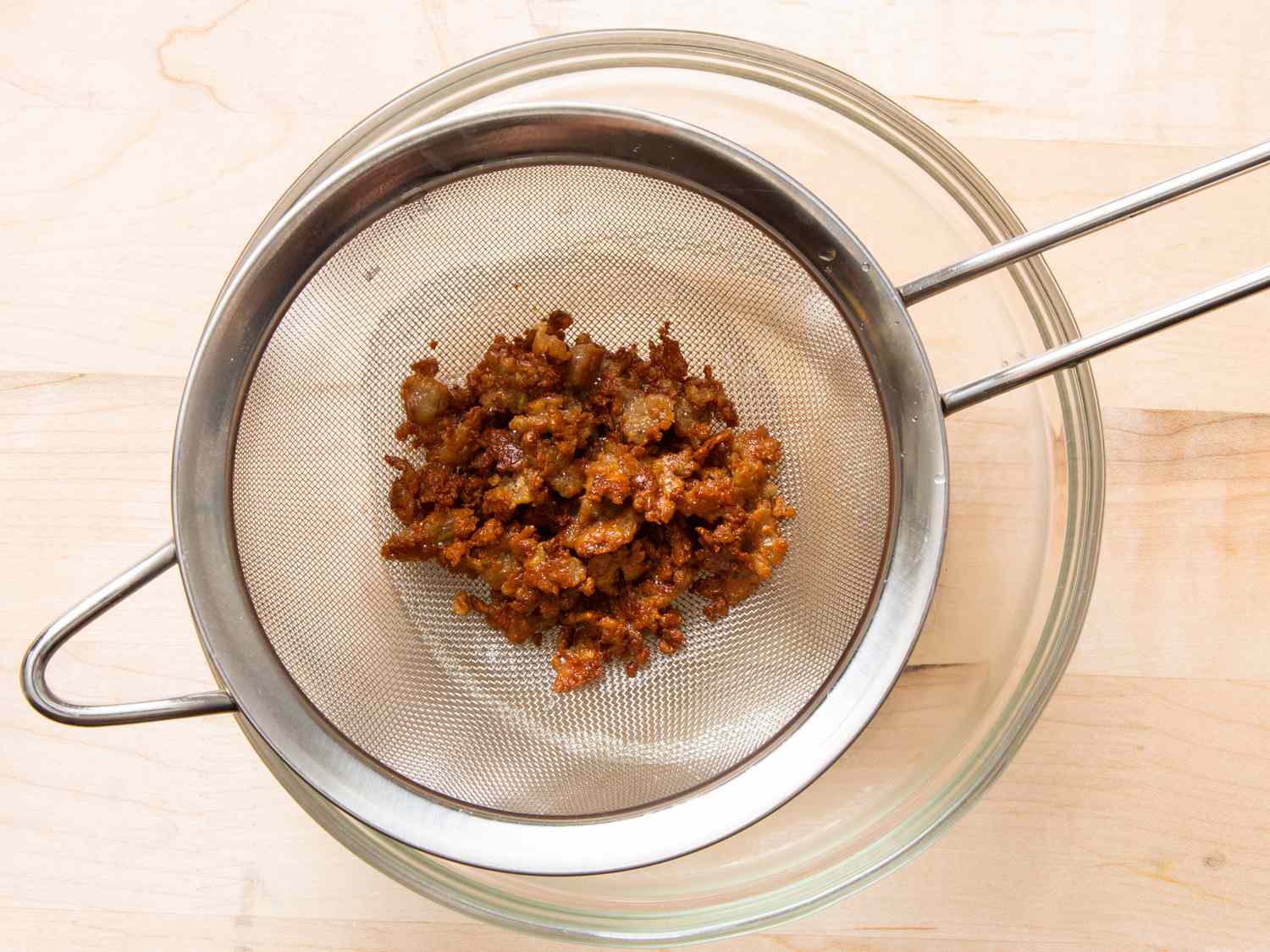 coconut cream curds sitting in a fine mesh strainer with oil reserved in bowl below