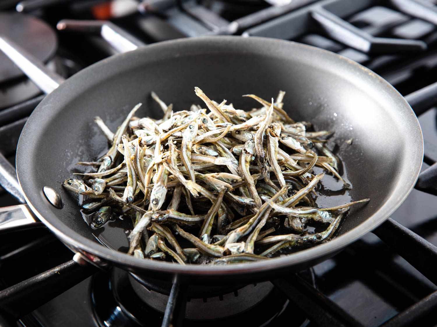 Baby anchovies are tossed with oil and cooked in a skillet.