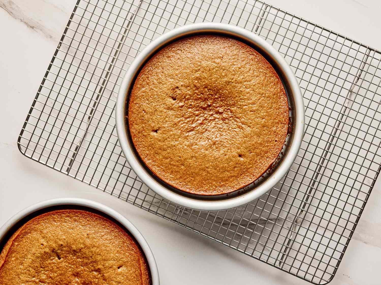 Two baked round cakes in pans on a cooling rack