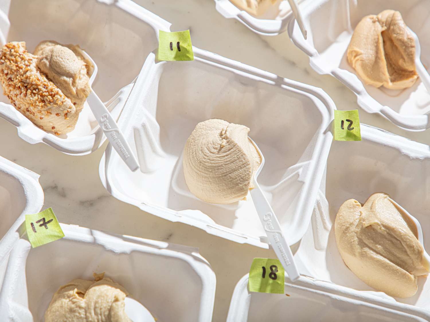 Various samples of hummus displayed in numbered containers with spoons