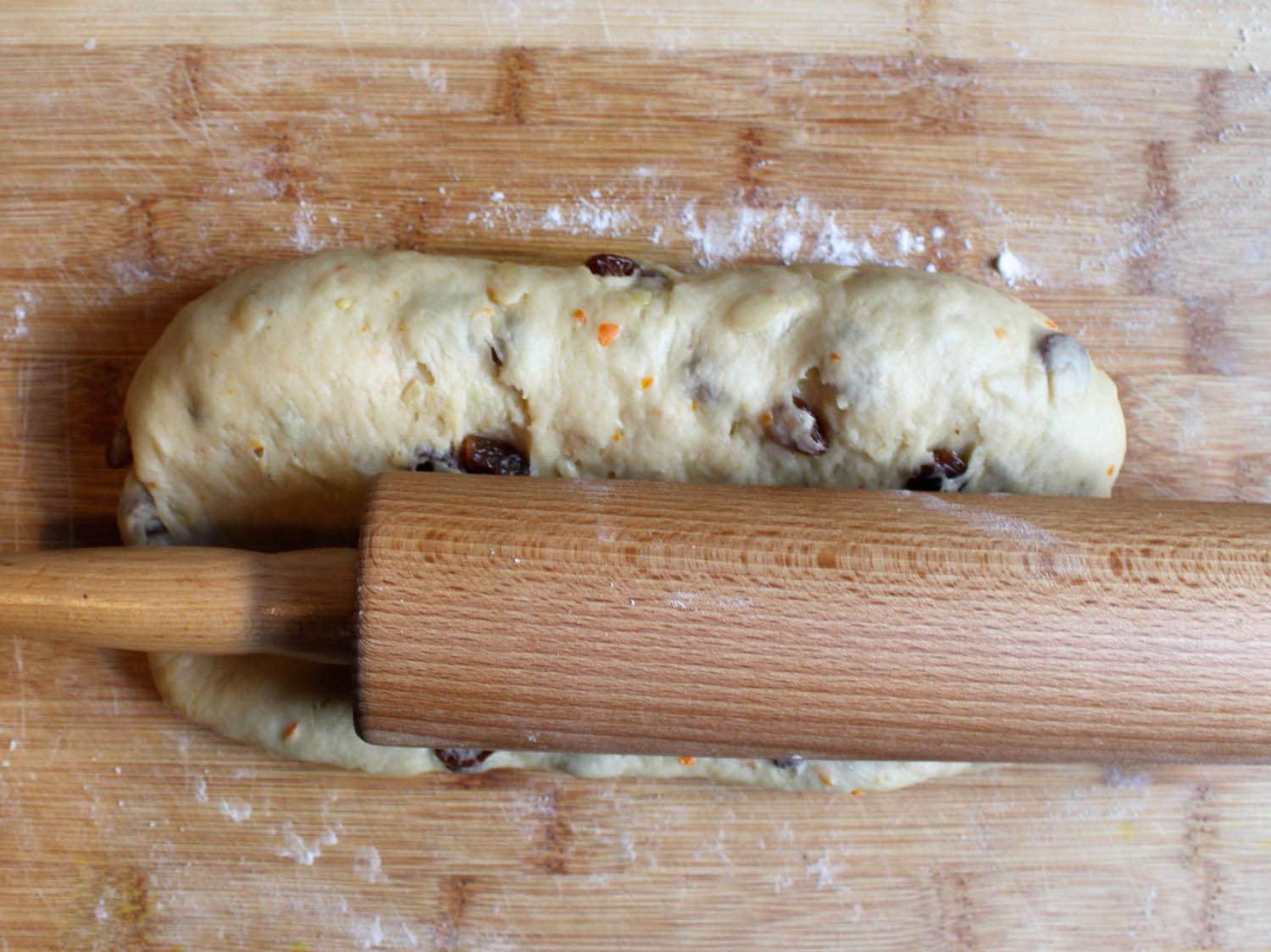 Using a rolling pin to make a trench for marzipan in uncooked stollen dough, on a wooden work surface.