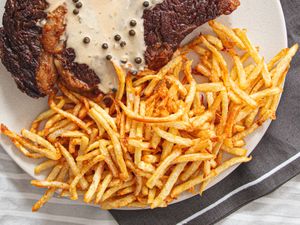 A steak with pepper sauce next to a serving of thincut fries on a plate