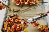 A person pulling grilled meat off of skewers.