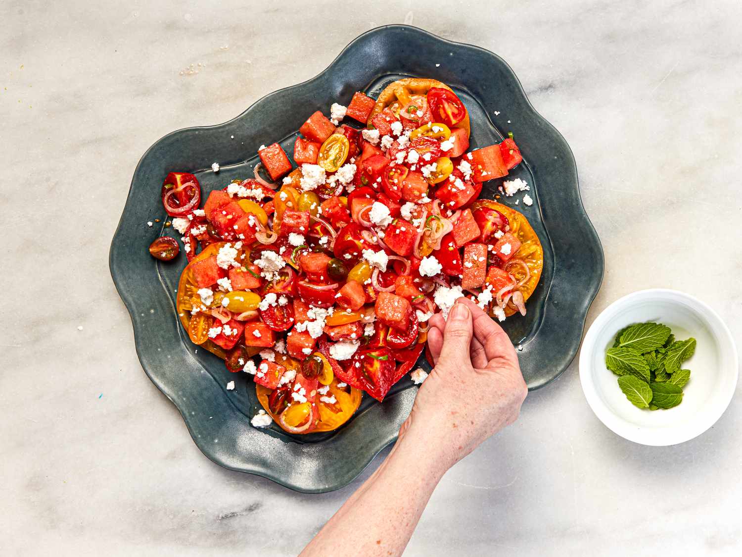 Sprinkling feta on a tomato-watermelon salad