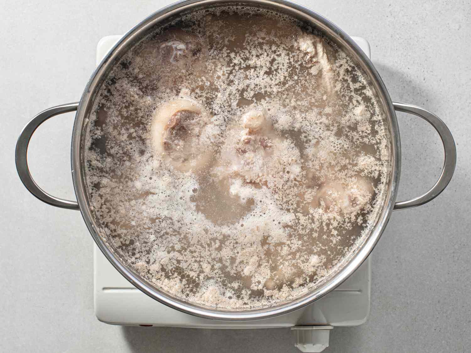 Pork and chicken bones coming to a boil with water in a large stockpot over high heat.