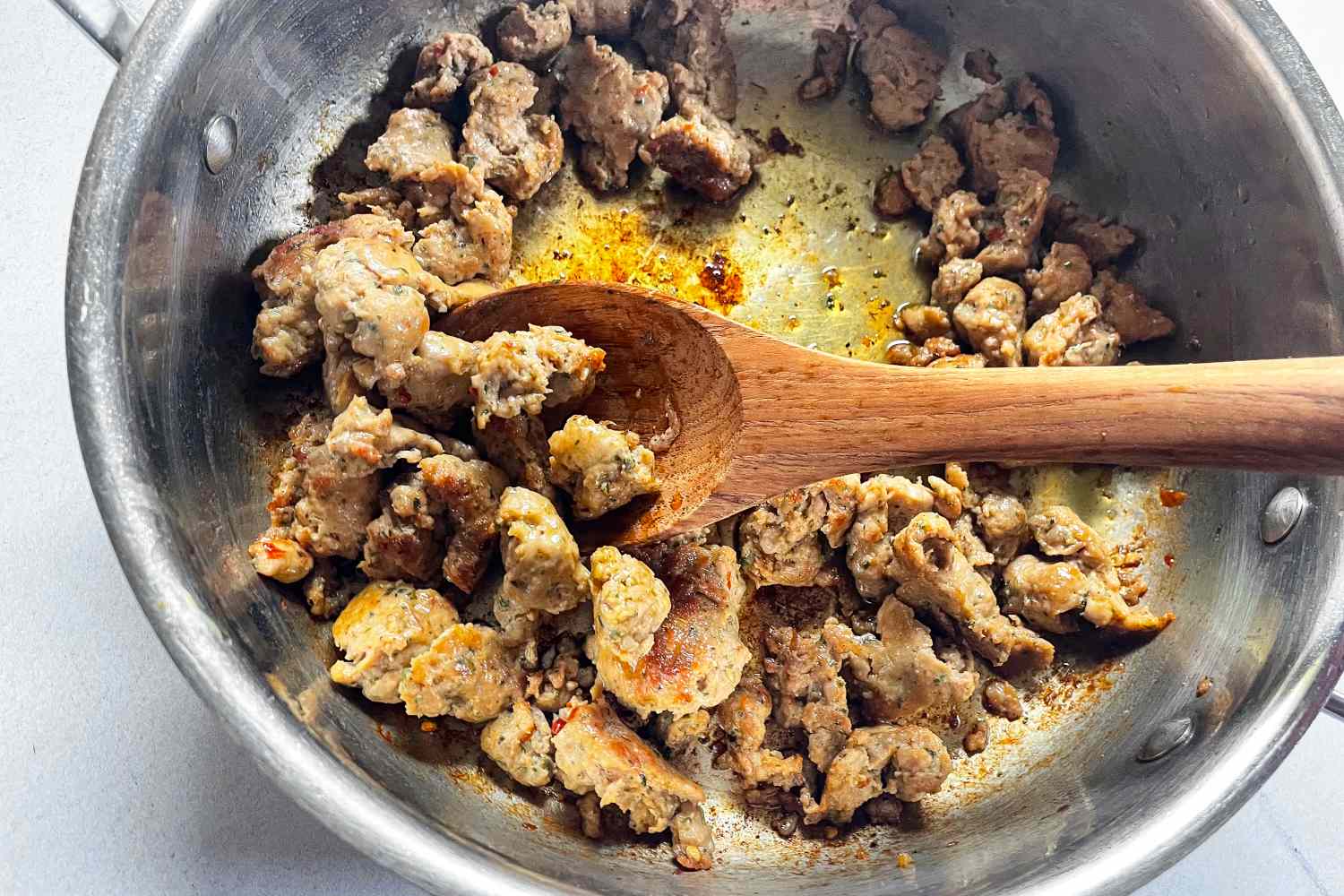 Cooked sausage pieces in a skillet with a FAAY Teak Cooking Spoon