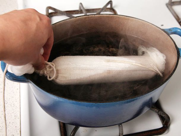 The cheese cloth-wrapped foie gras torchon is lowered into an oval Dutch oven full of steaming water.
