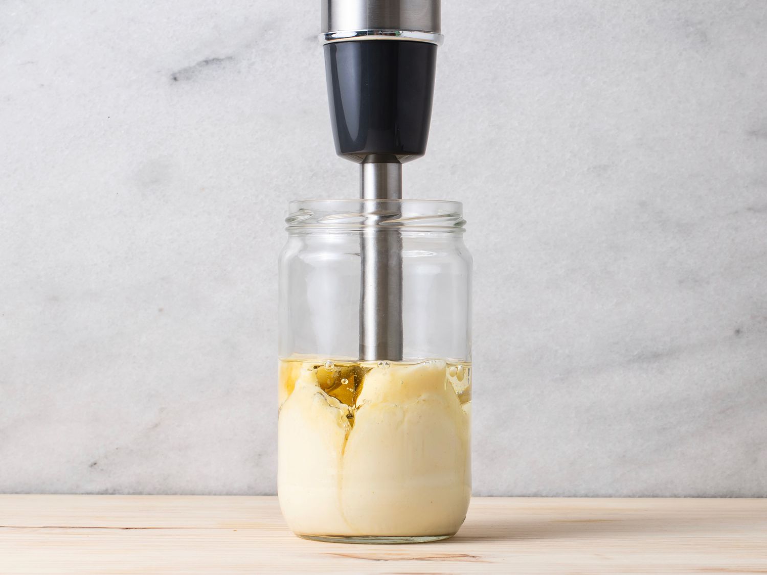 The mayonnaise ingredients being emulsified with the immersion blender, highlighting how the blender pulls the oil down from the surface.