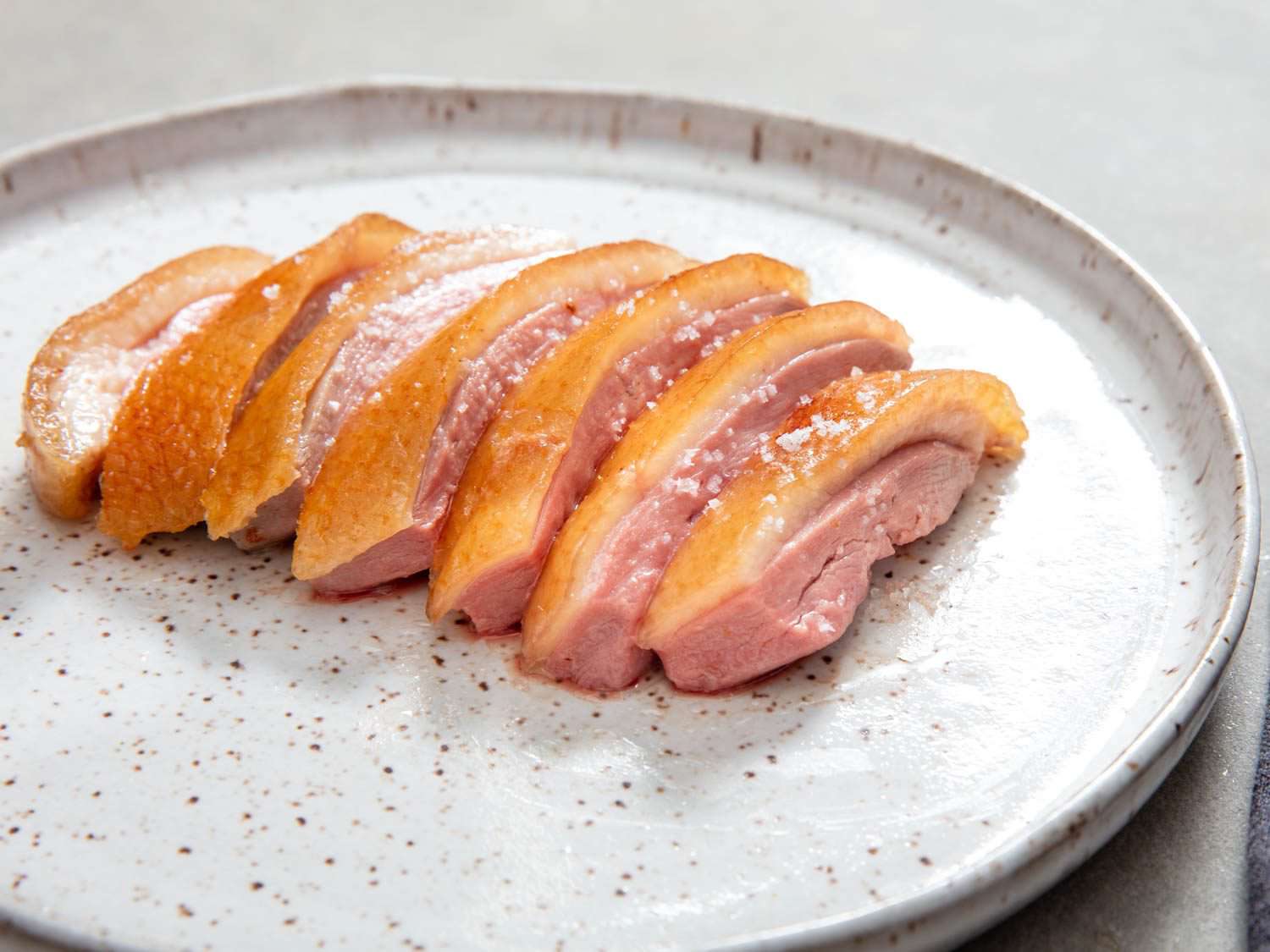 Side view of sliced roast duck breast, cooked to a rosy medium, on a dinner plate.