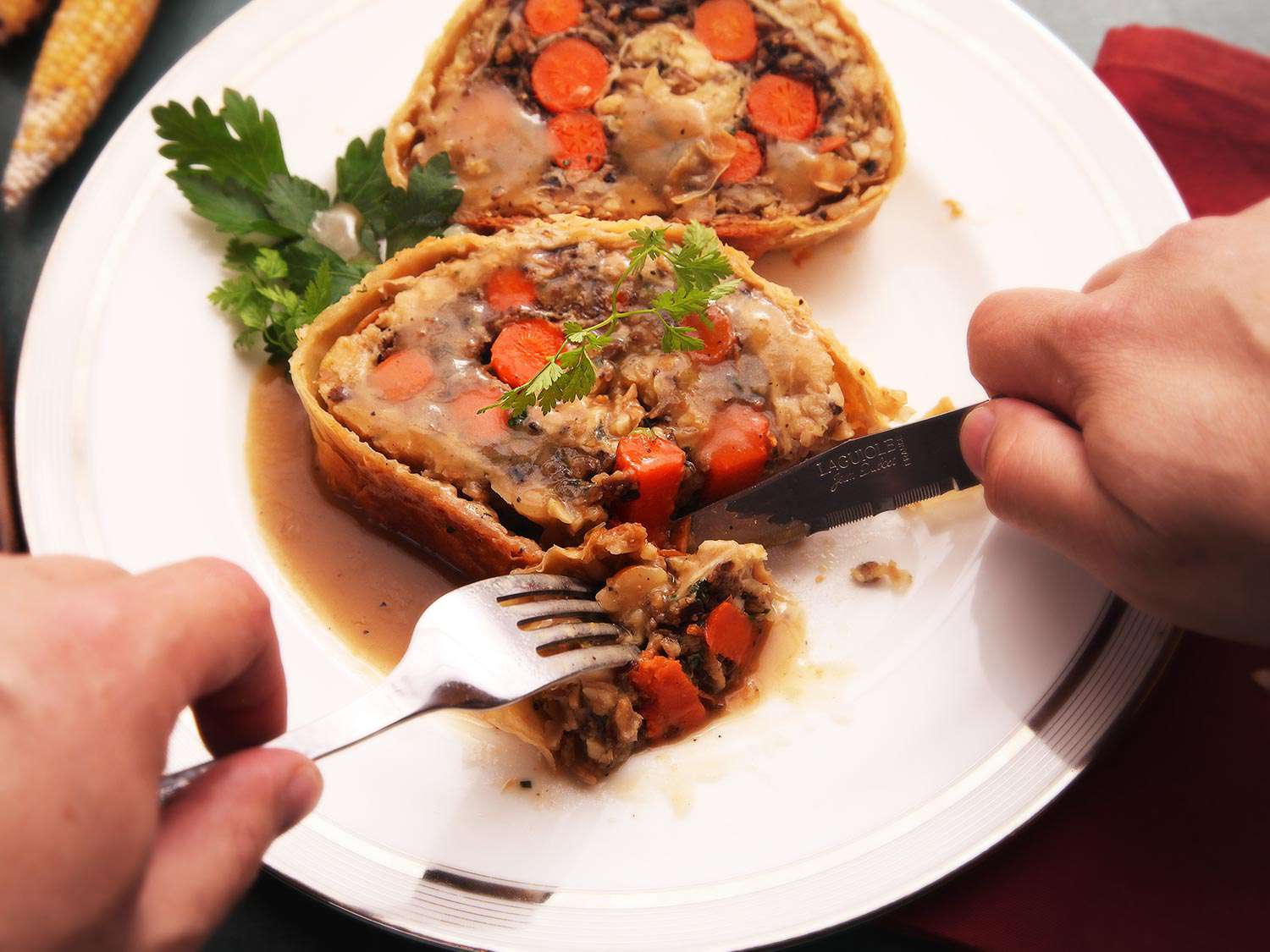 Cutting a bite of gravy-soaked of vegetables Wellington.
