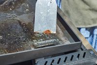 A person cleans the top of the Weber Slate 30 Inch Griddle with a spatula