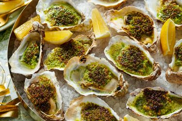Roasted oysters topped with herbs and seasoning arranged on a platter with lemon wedges