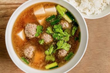 A white porcelain bowl holding the Thai pork and tofu soup. On the top righthand of the image is a bowl of white rice.