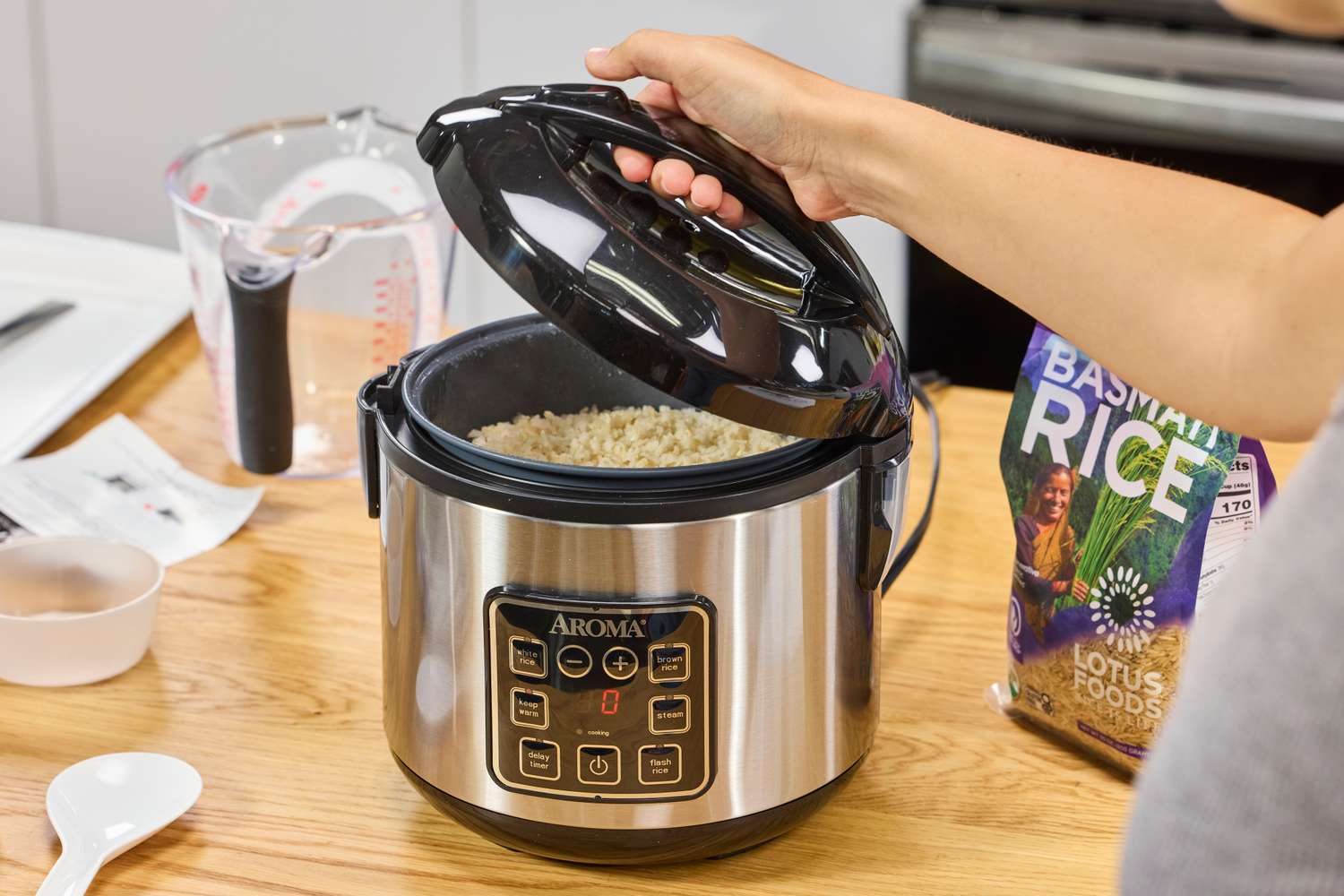 A person opens the lid on the Aroma Housewares 8-Cup Rice and Grain Cooker