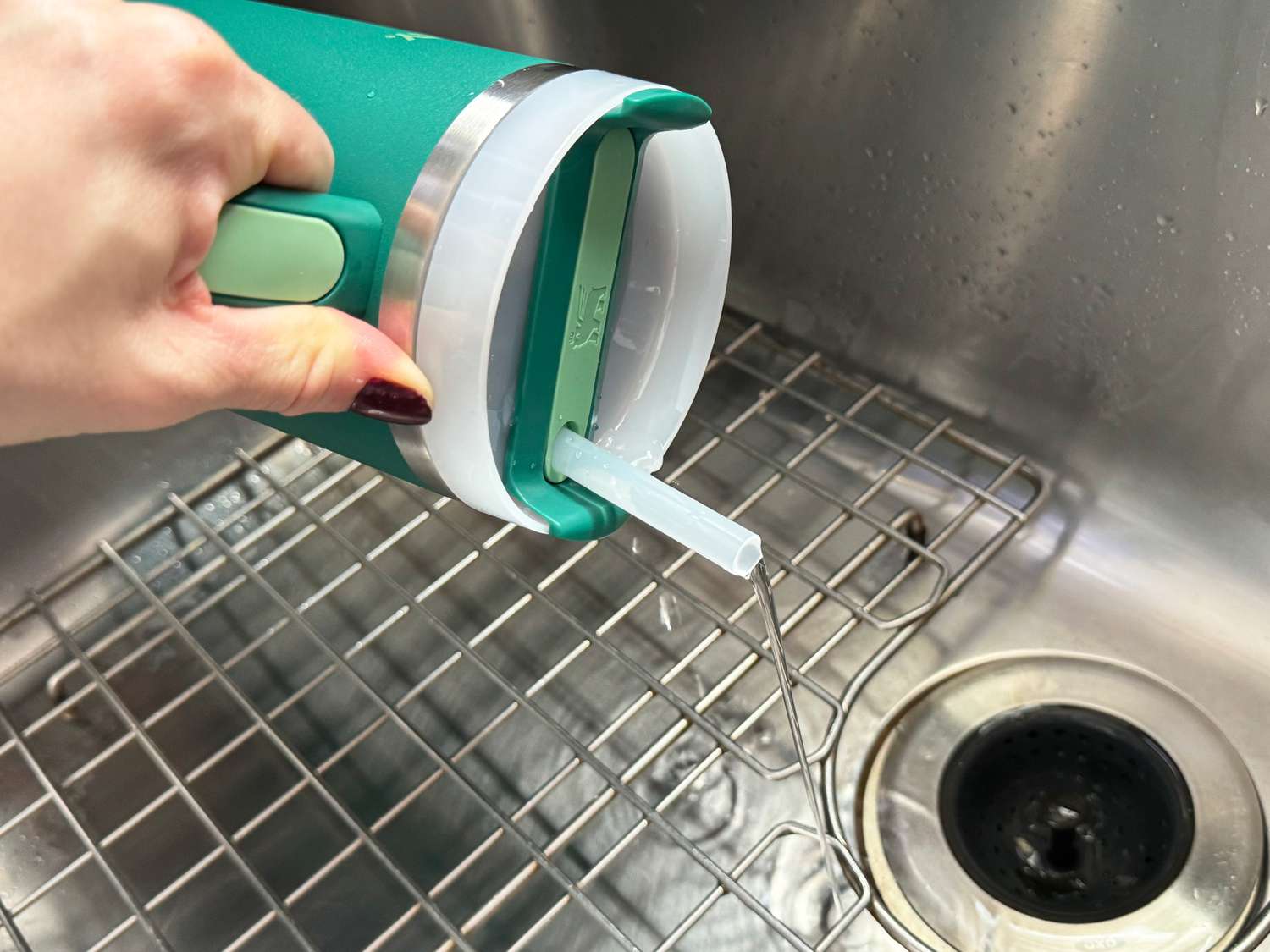 A person holding an insulated tumbler over the sink was water pours our of its lid.