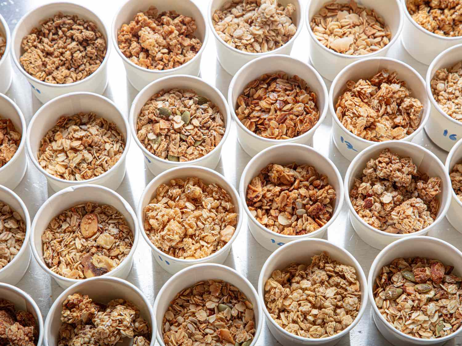 A collection of paper cups each filled with various types of granola organized in a gridlike pattern