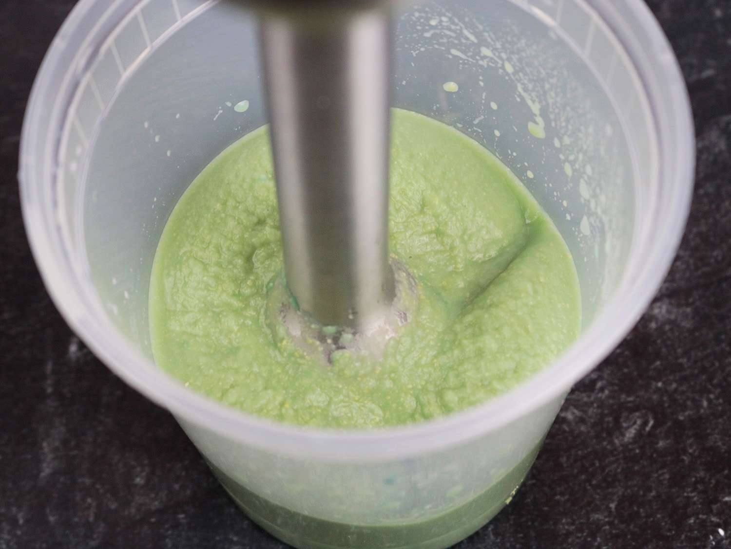 An immersion blender pureeing chickpeas and drops of blue food coloring to see how quickly they incorporate