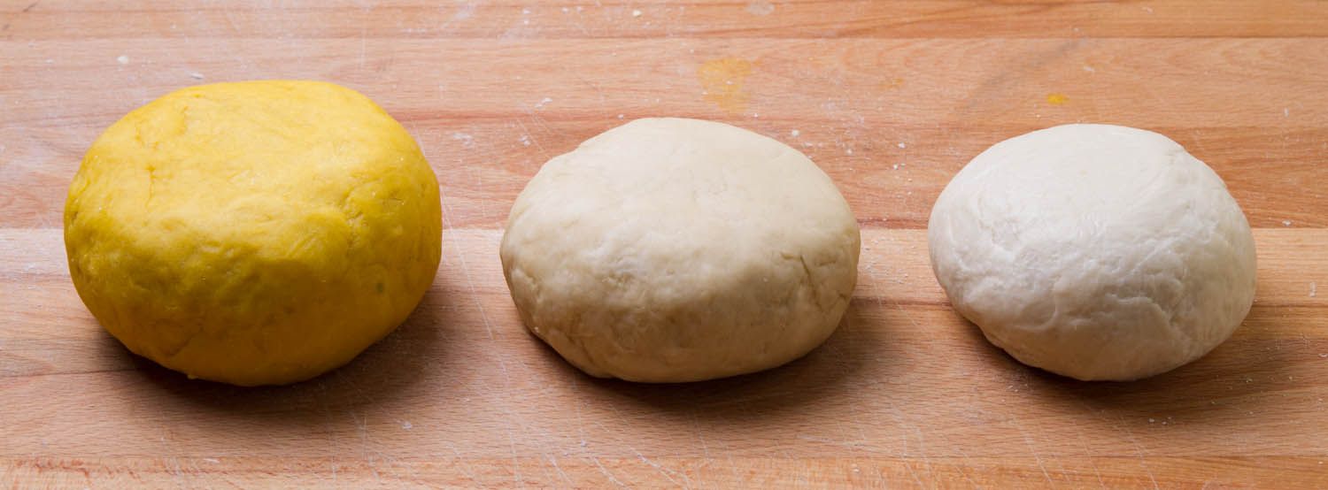 Three balls of pasta dough, one made with egg yolks, one made with egg whites, and one made with flour and water only.