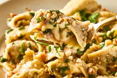 A closeup of a fork lifting a stuffed pasta piece from a dish of agnolotti with garnish