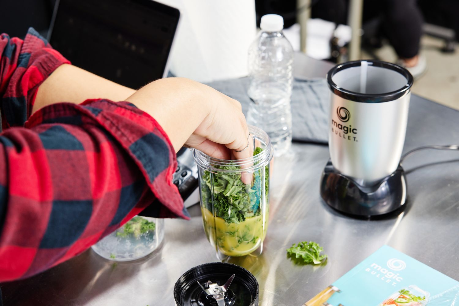 A person preparing ingredients in a cup for a Magic Bullet blender on a kitchen counter