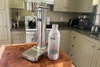 The Aarke soda maker with a bottle of sparkling water next to it