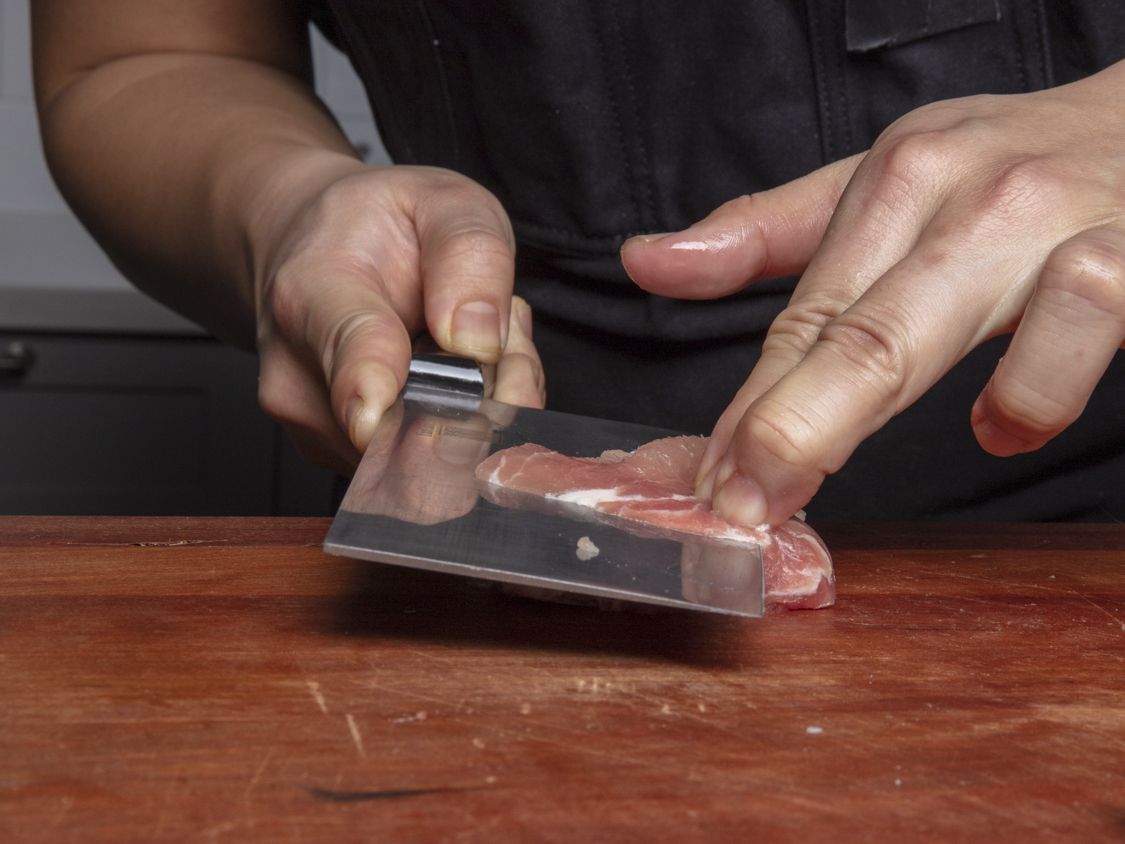 A knife going through a piece of pork at a horizontal angle. 
