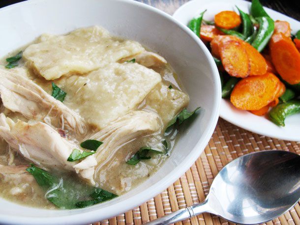 A soup bowl with a helping of chicken and slick dumplings. Sautéed carrot slices and snap peas are piled on a plate nearby.