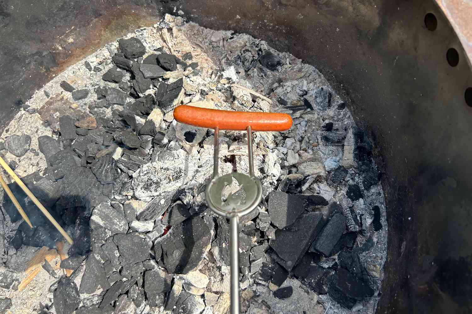 A a hot dog being cooked on a skewer over a fire pit.