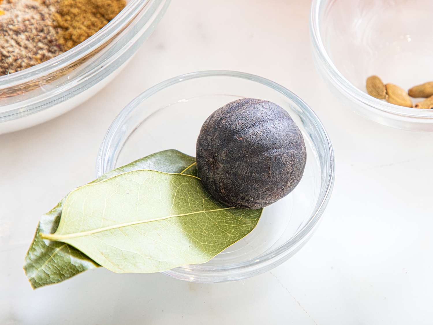 A dried lime and a bay leaf in a small glass dish part of ingredients for cooking