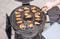 A person removes chicken from the Char-Griller E16620 Akorn Kamado Charcoal Grill