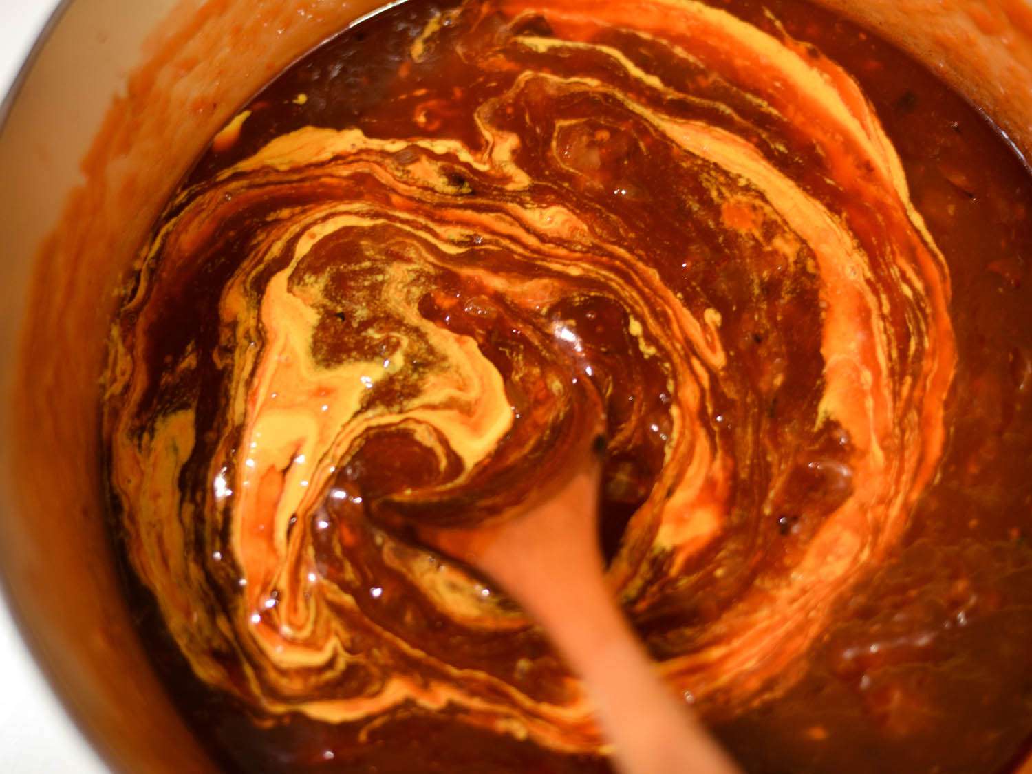 Wooden spoon stirring mustard into a pot of barbecue sauce