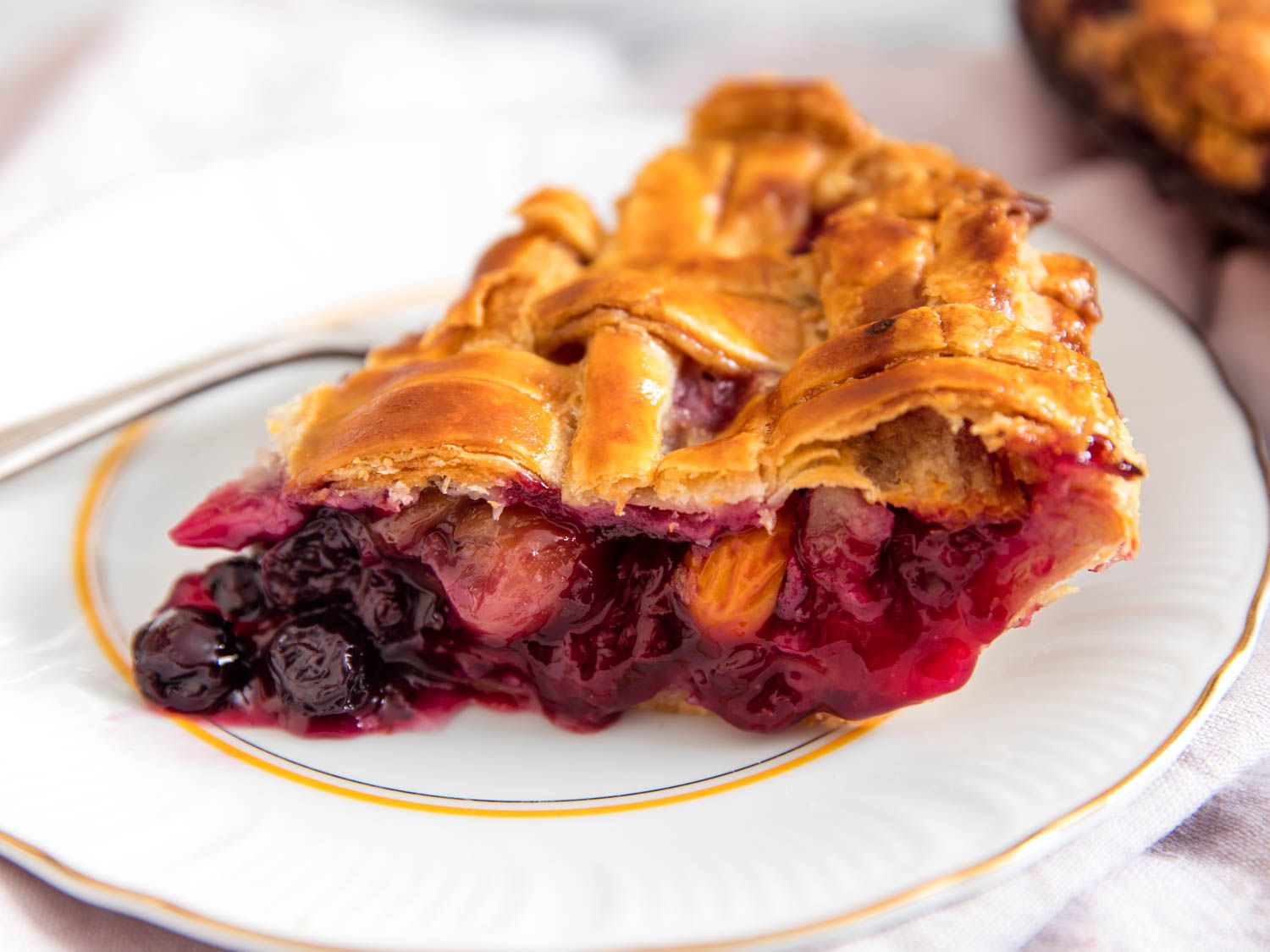 A close-up of a slice of the pie on a plate. The exposed filling on the side facing the camera is studded with tender berries.