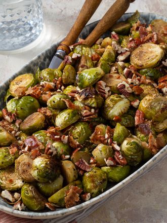 Brussels sprouts in a ceramic serving dish with tongs, a napkin, and glass cups on the periphery