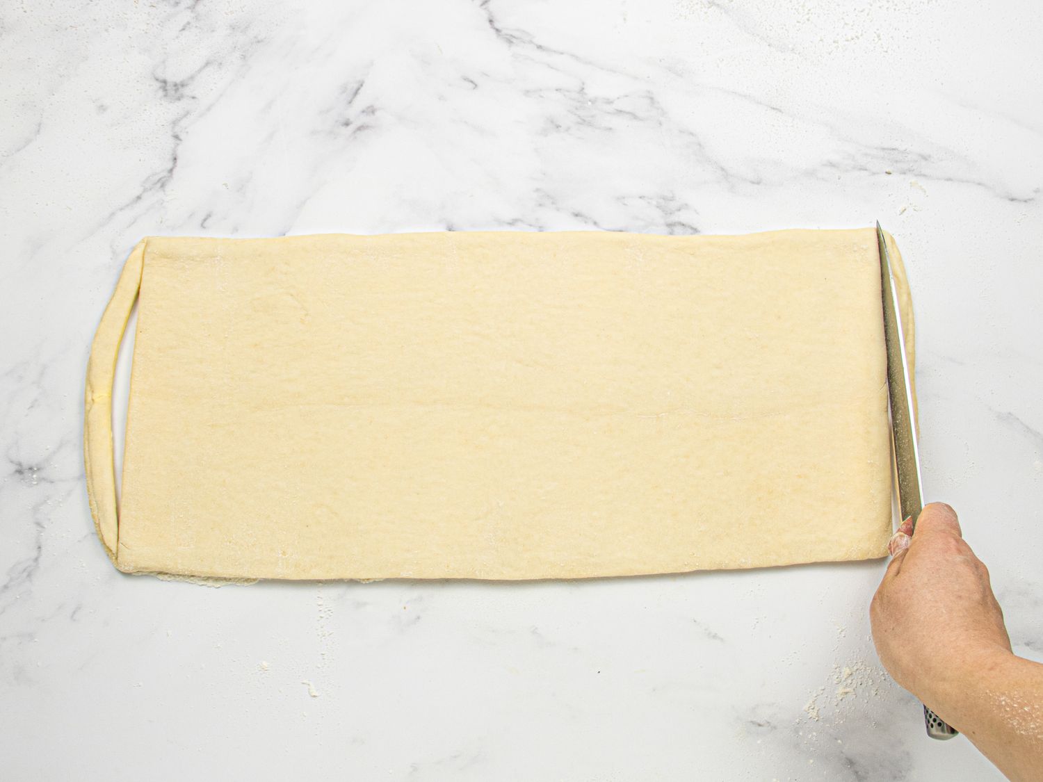 A hand cutting a sheet of dough on a marble surface