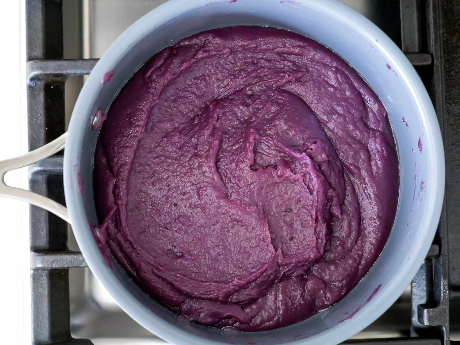 Overhead view of ube cooking and thickening in a saucepan.