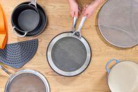 a person placing the le creuset splatter screen on a skillet
