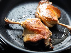 Two duck confit legs in a skillet. 