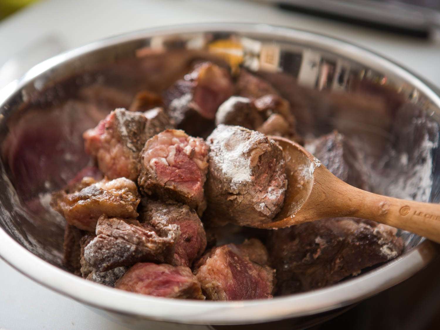 Tossing cubed beef in flour to form light paste