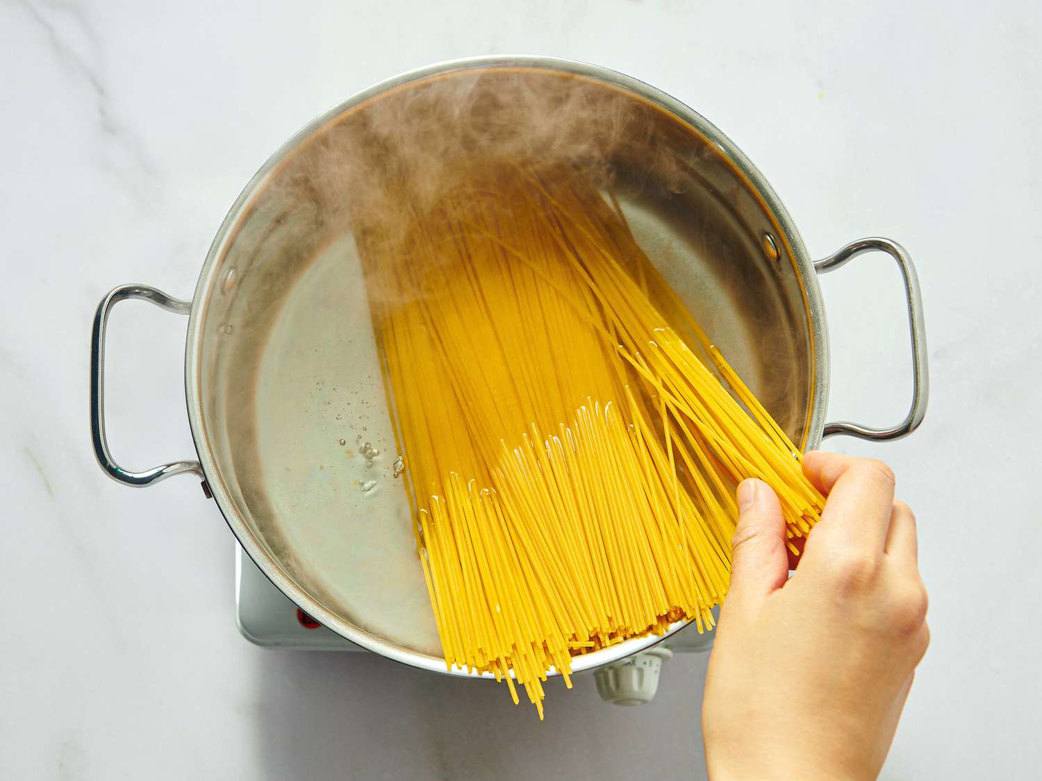 Hand placing dry spaghetti into a pot of boiling water on a kitchen stove