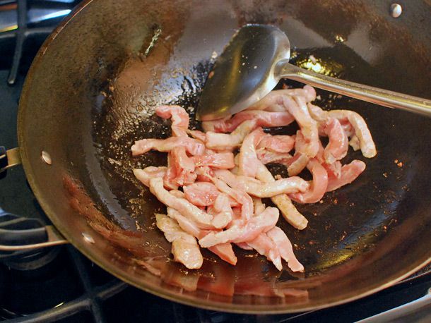 Stir-frying marinated pork loin strips in a hot wok with oil