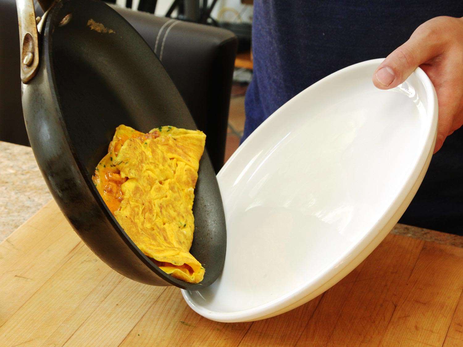 A cooked omelette being transferred from the pan to a plate.