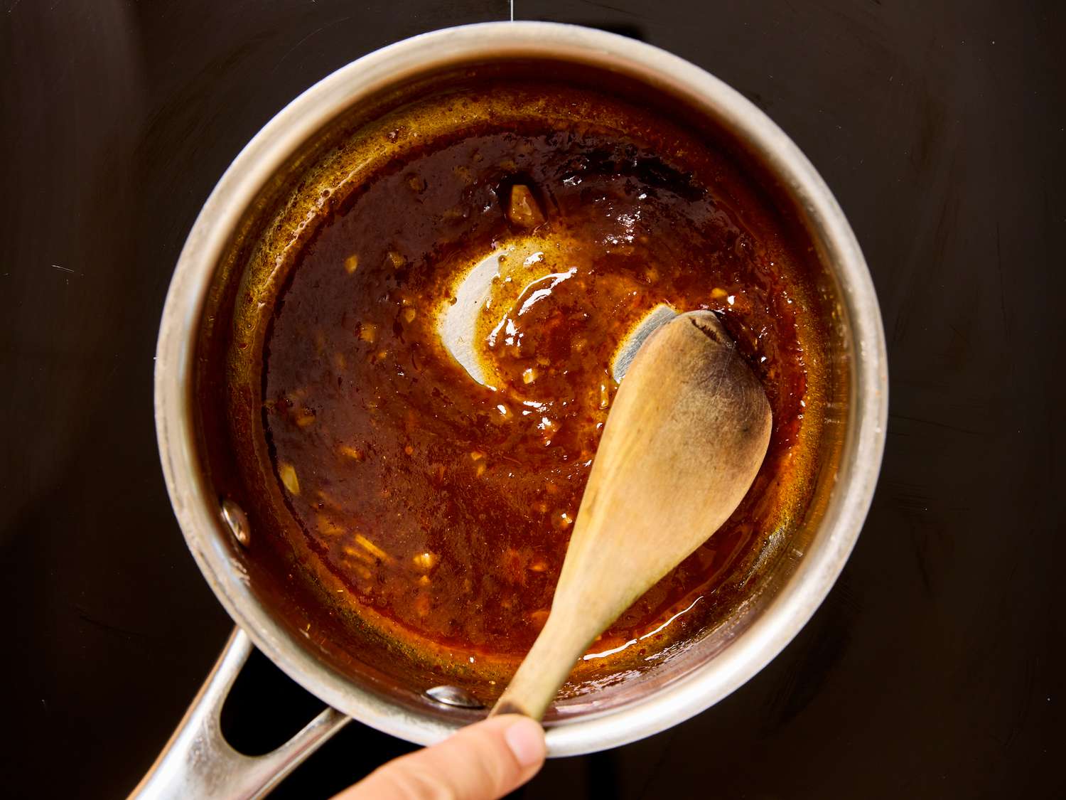 A saucepan with honey harissa glaze being stirred using a wooden spoon