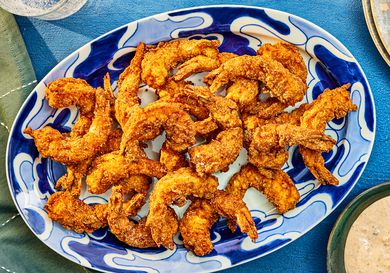 Southern Fried Shrimp on a blue printed plate, with dip, and sparkling water, and a blue textile. 