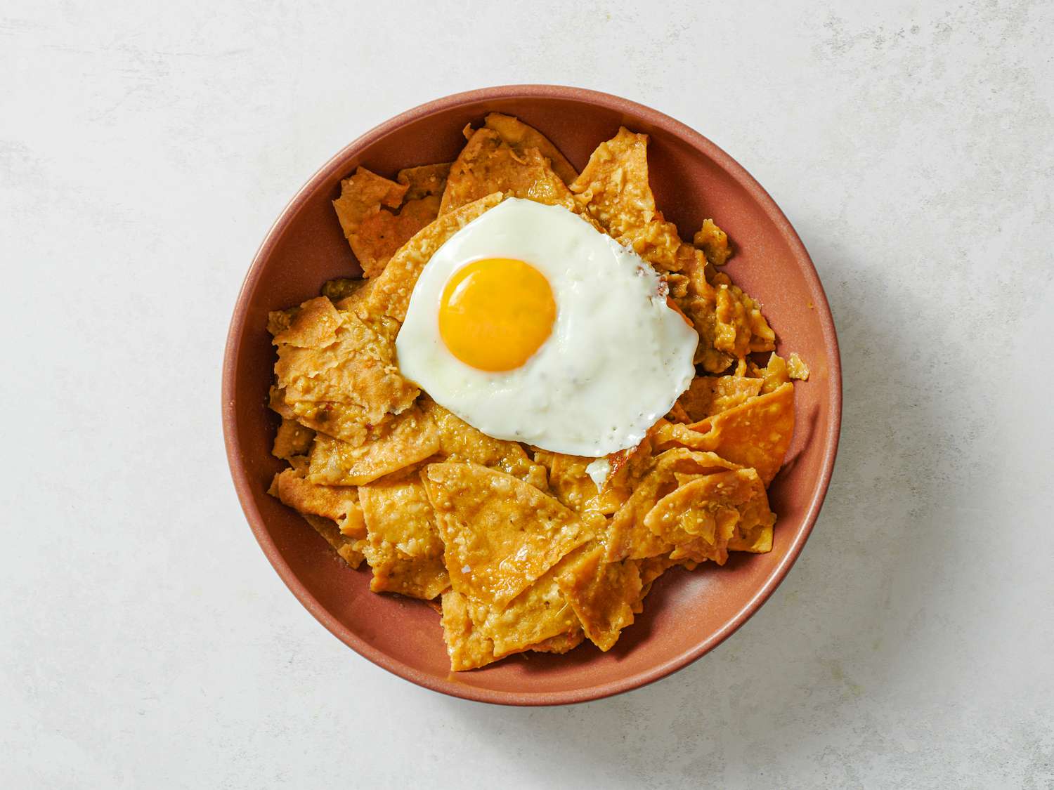 A pink bowl holding salsa-coated tortilla chips, topped with a fried egg.