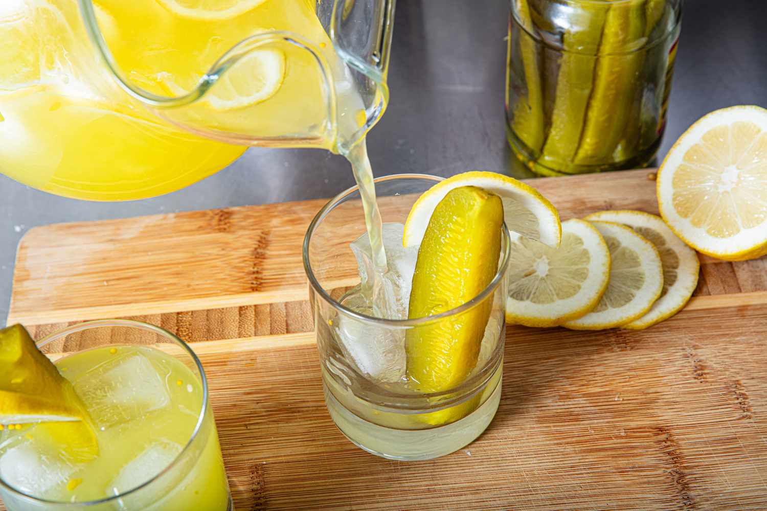 A glass of lemonade with a pickle being poured from a pitcher