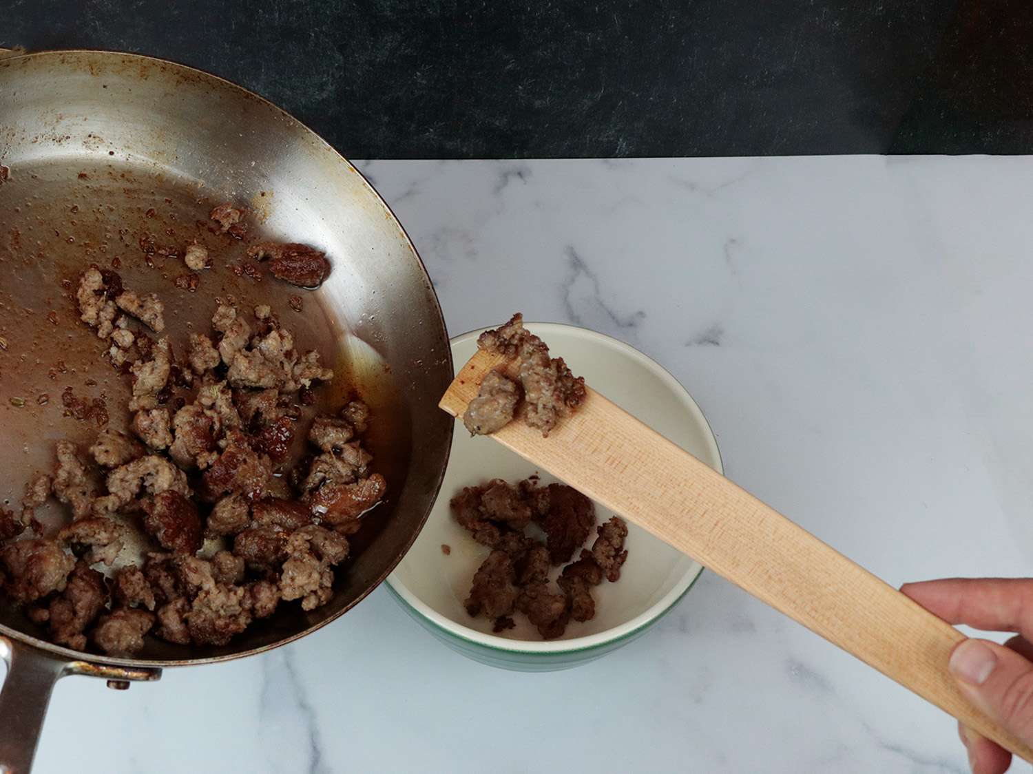 a flat wooden paddle scooping sausage into a bowl 