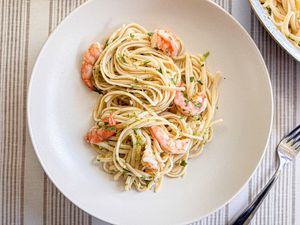 A plate with spaghetti and shrimp, garnished with herbs, placed on a table with a fork nearby